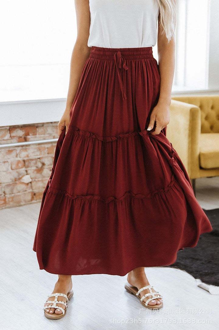Woman wearing a flowy burgundy tiered maxi skirt with a white sleeveless top and white sandals indoors