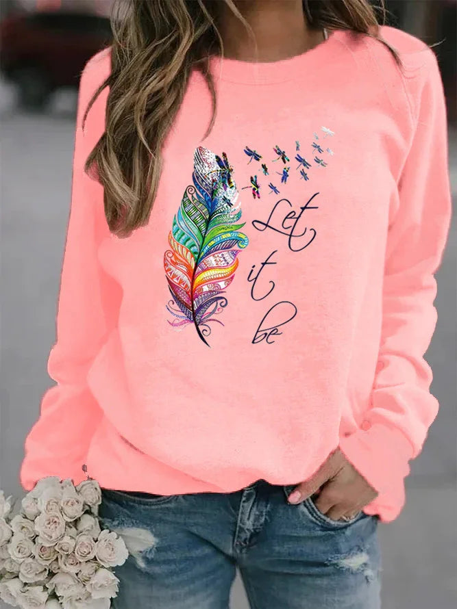 Woman wearing pink sweatshirt with colorful feather and dragonflies graphic and 'Let it be' text