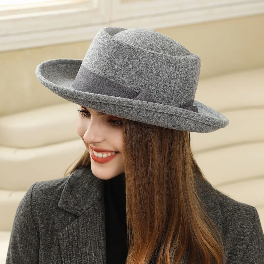 Smiling woman wearing a gray felt fedora hat and dark gray coat indoors