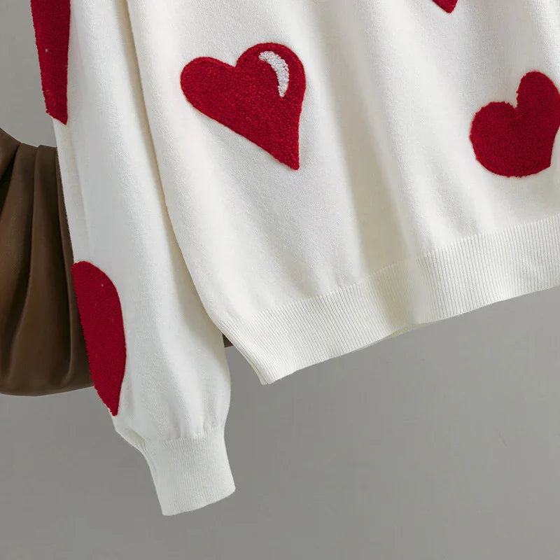 White sweater with red textured heart patterns on sleeve and body, featuring ribbed cuffs and hem