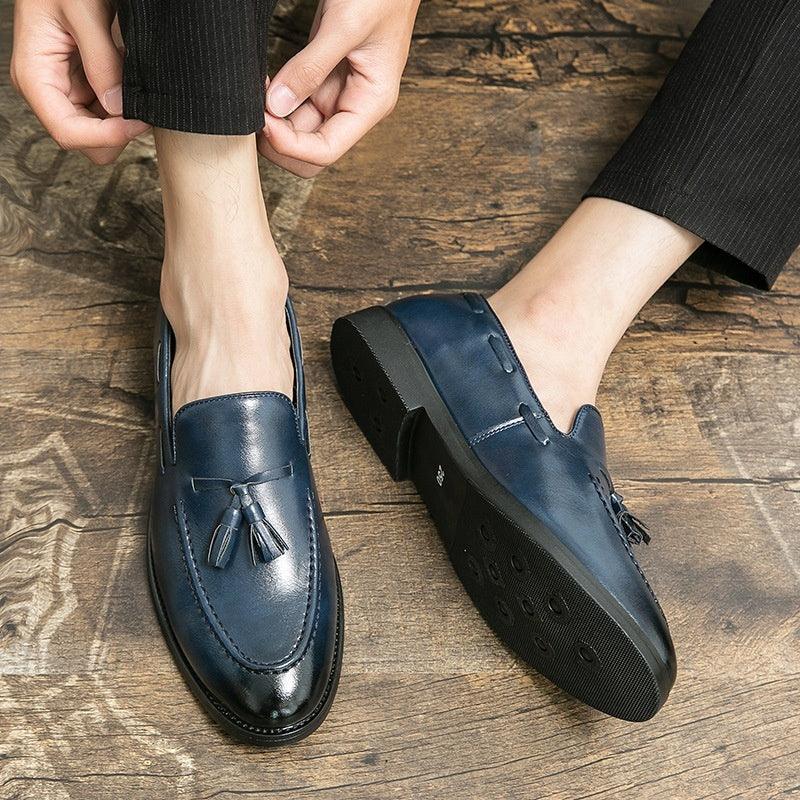 Close-up of navy blue leather tassel loafers worn with black pinstripe pants on wooden floor