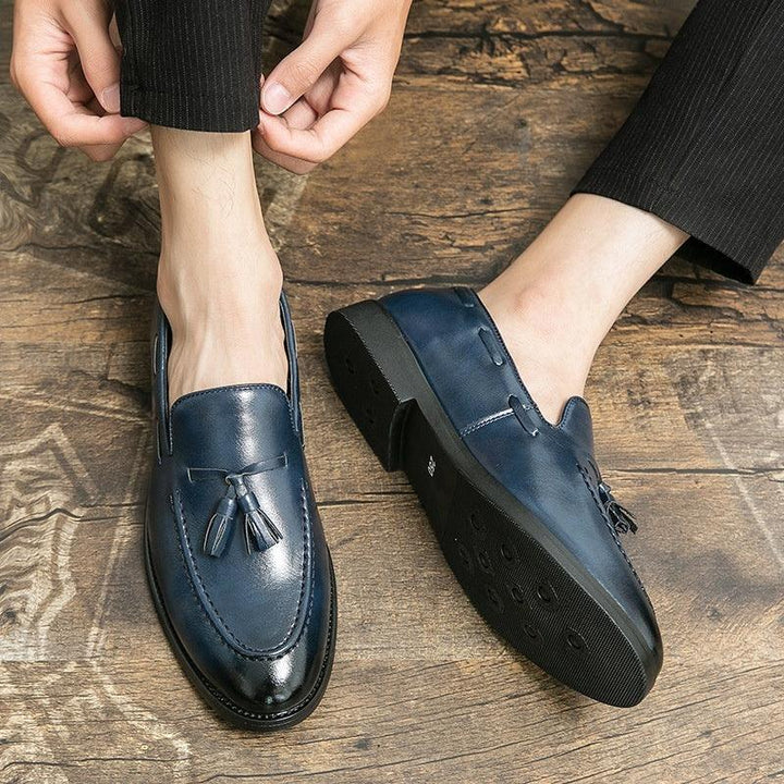 Close-up of navy blue leather tassel loafers worn with black pinstripe pants on wooden floor