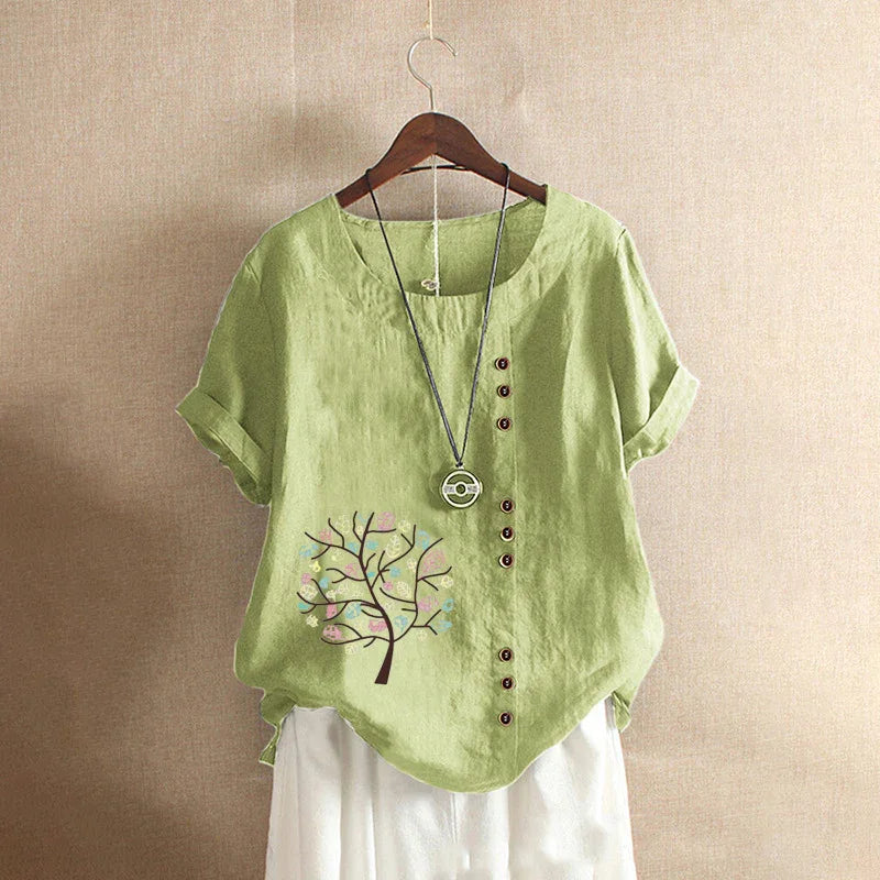 Light green linen short sleeve blouse with tree print, asymmetrical buttons, and pendant necklace