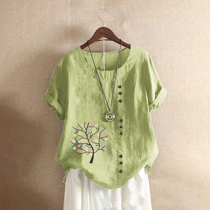 Light green linen short sleeve blouse with tree print, asymmetrical buttons, and pendant necklace