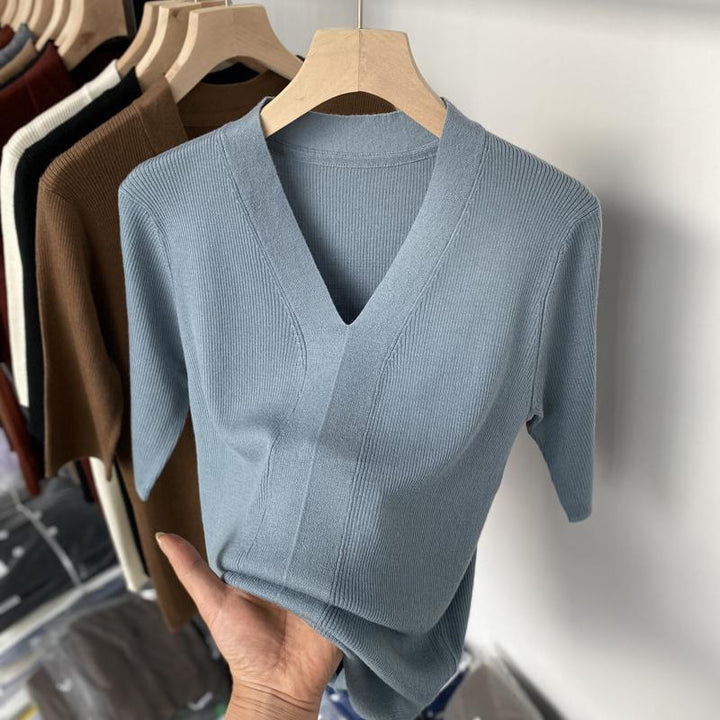 Hand holding light blue ribbed V-neck short sleeve top on wooden hanger with other sweaters in background