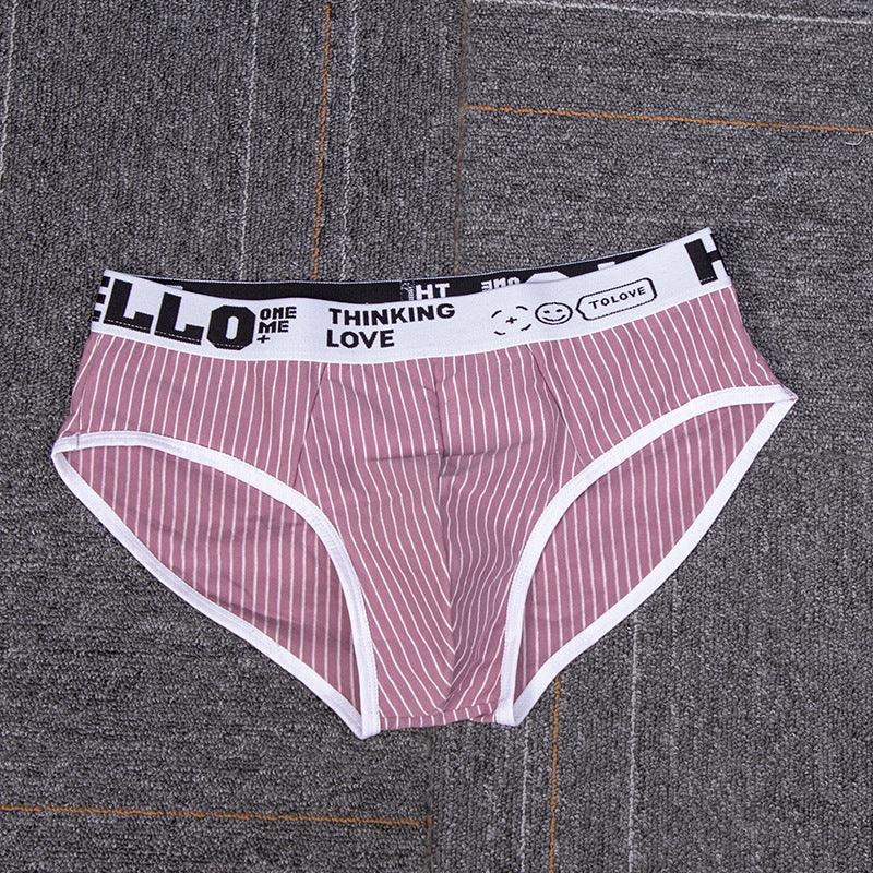 Pink striped men's briefs with white waistband featuring black text and smiley face on gray carpet