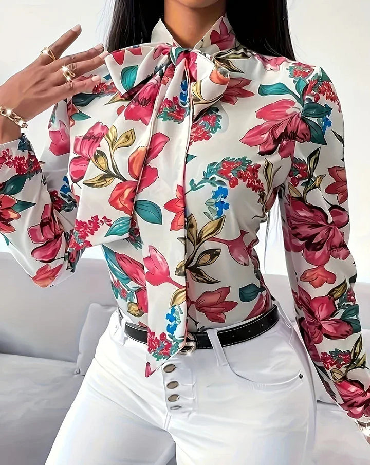 Woman wearing white floral blouse with large bow and white high-waisted pants with black belt