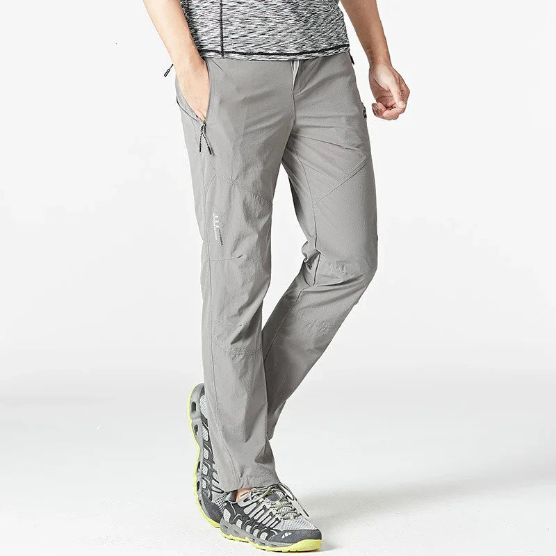 Man wearing light grey outdoor hiking pants and black grey sports shoes on white background