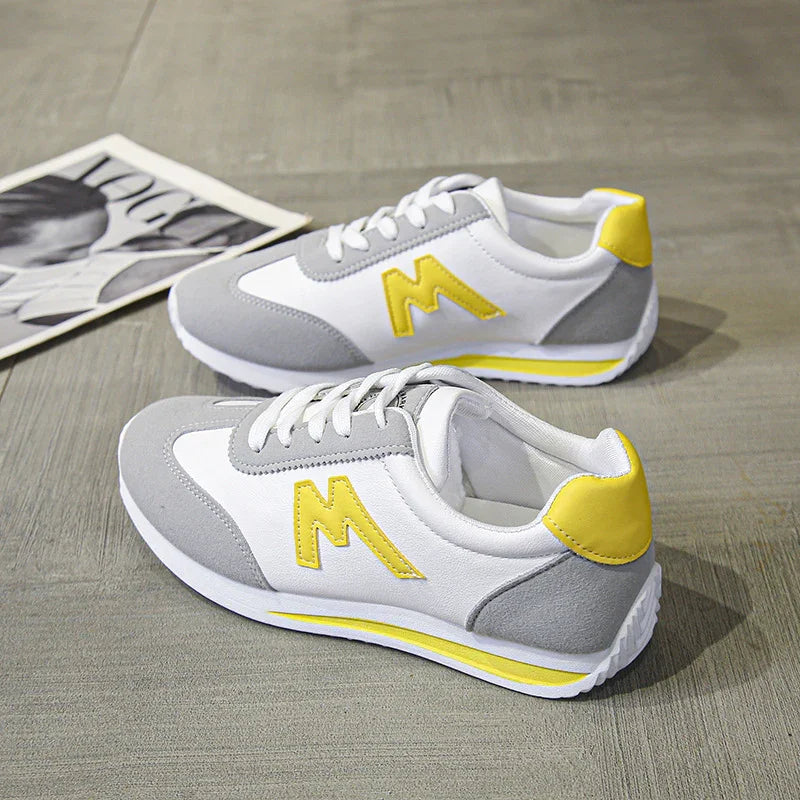 Pair of white, gray, and yellow casual sneakers with lace-up design on wooden floor