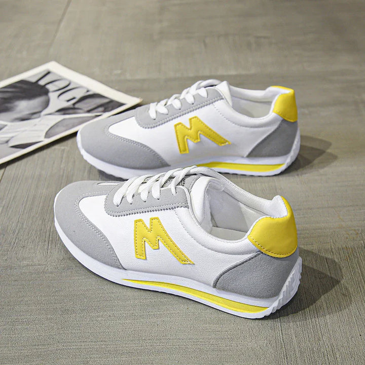 Pair of white, gray, and yellow casual sneakers with lace-up design on wooden floor