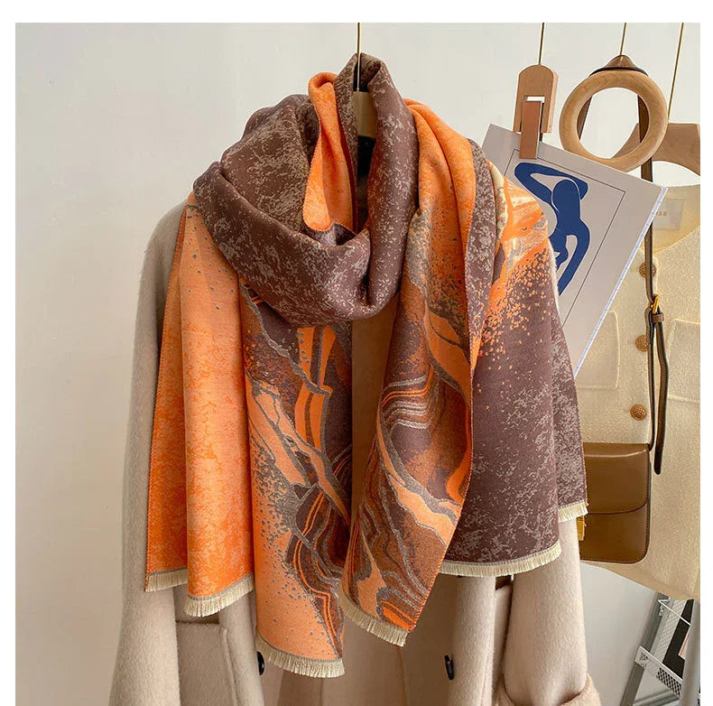 Orange and brown abstract patterned scarf draped over beige coat on wooden hanger