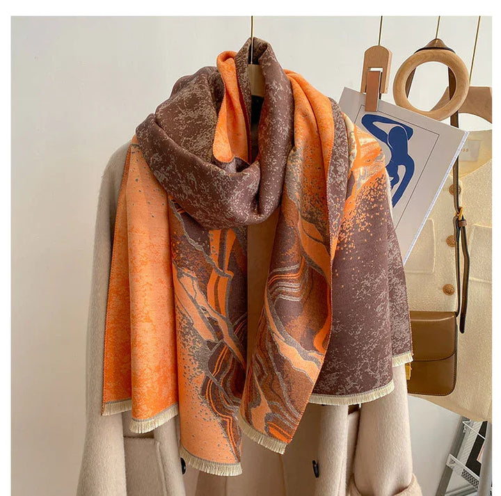 Orange and brown abstract patterned scarf draped over beige coat on wooden hanger