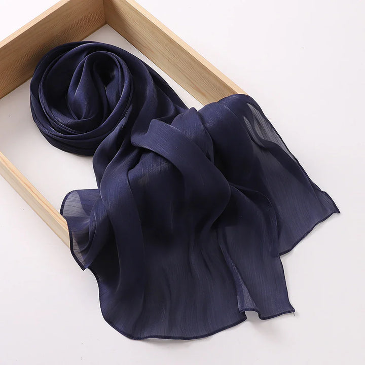 Elegant navy blue sheer chiffon scarf folded and displayed in a wooden tray on white background