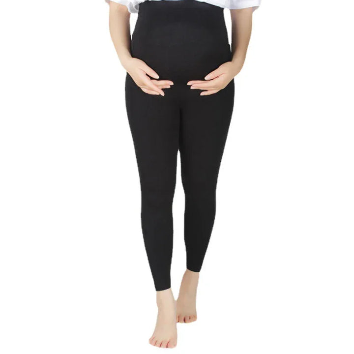 Pregnant woman wearing black maternity leggings, hands gently holding belly, white background