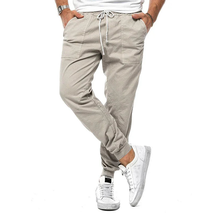Man wearing beige jogger pants with drawstring waist and white sneakers on white background