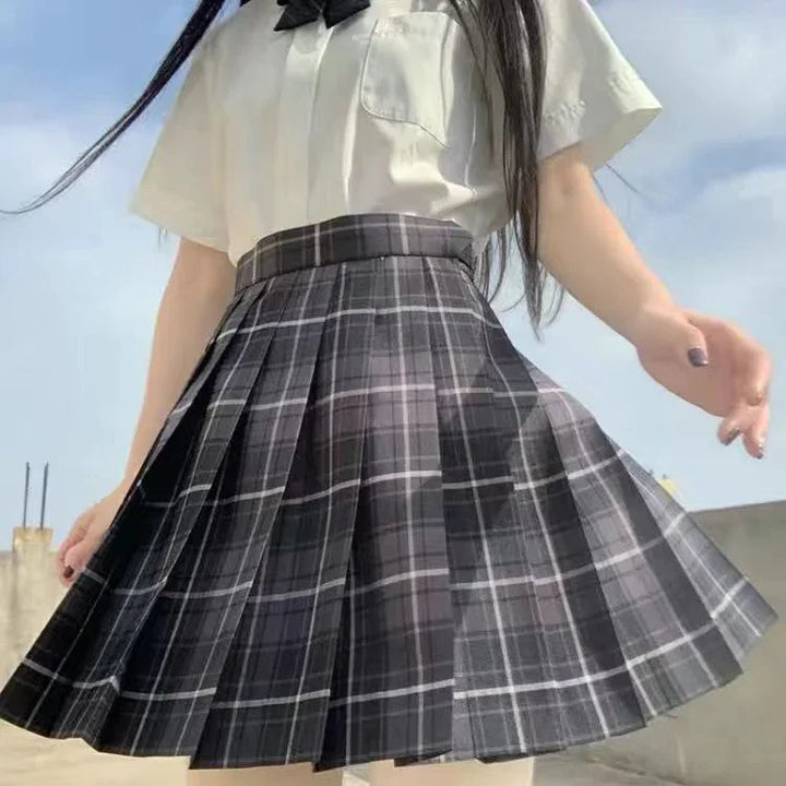 Young woman wearing pleated black and gray plaid skirt and white blouse outdoors under blue sky