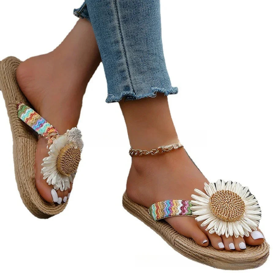Feet wearing colorful woven sandals with large daisy flower decoration and ankle bracelet