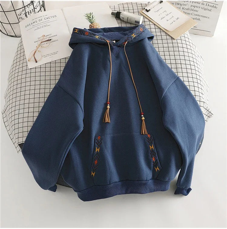Navy blue hooded sweatshirt with embroidered geometric patterns and tassel drawstrings on bed with checkered sheet