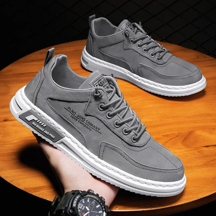 Pair of gray casual sneakers with white soles on wooden surface, featuring lace-up design and branded details