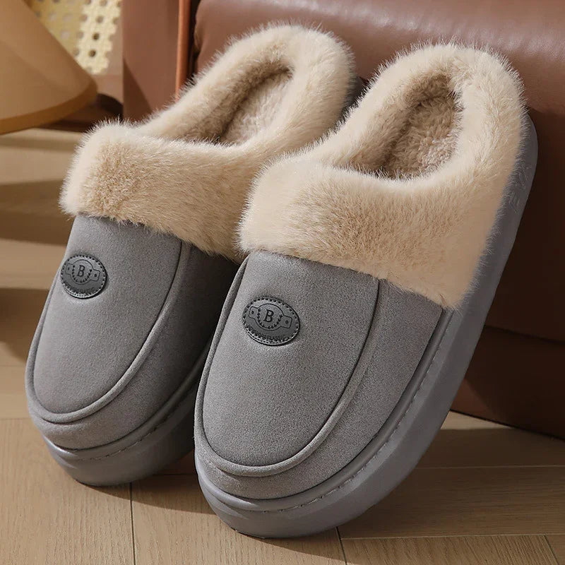 Gray cozy slippers with soft beige fur lining and black logo on wooden floor