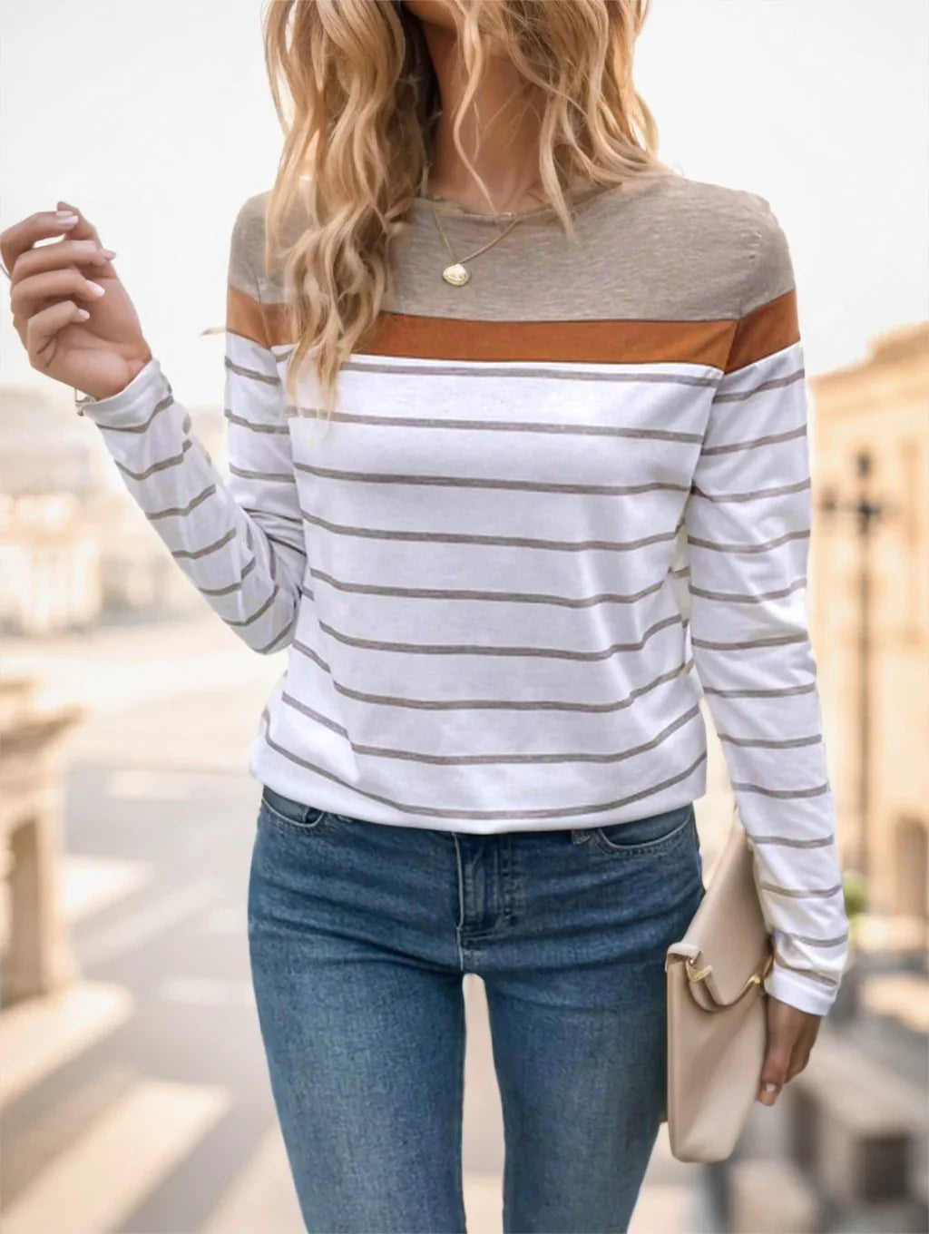Woman wearing a casual striped long-sleeve top with brown and gray accents, blue jeans, holding a beige clutch