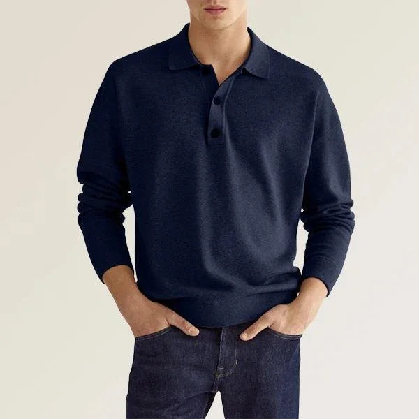 man wearing navy blue long sleeve polo sweater paired with dark blue jeans against neutral background