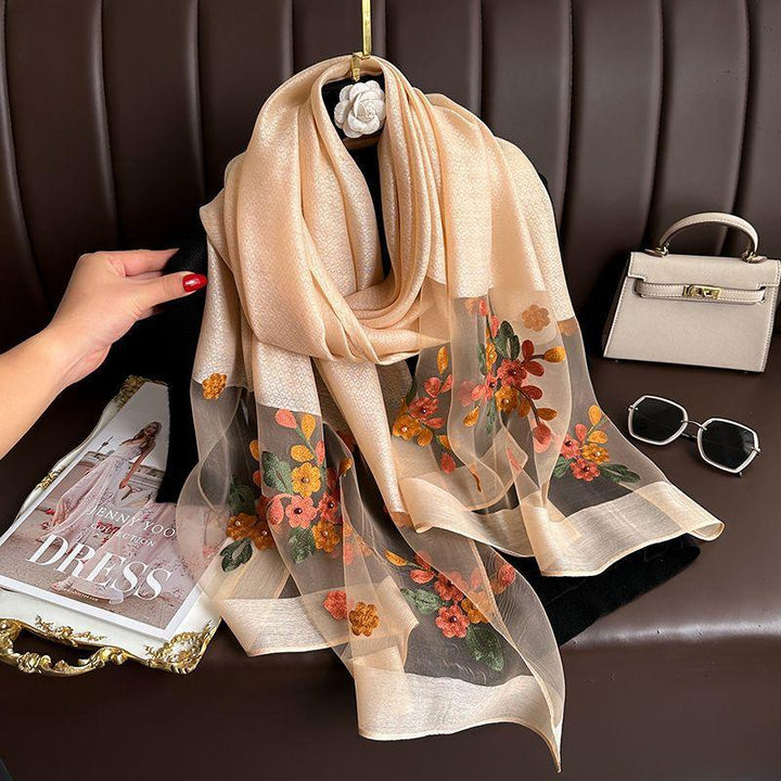 Beige floral embroidered scarf on black hanger with a beige handbag, sunglasses, and fashion magazine on brown leather sofa
