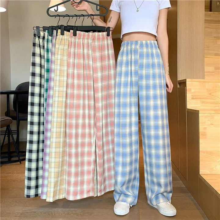 Woman wearing blue plaid loose pants holding a rack of multicolor plaid pants in casual indoor setting