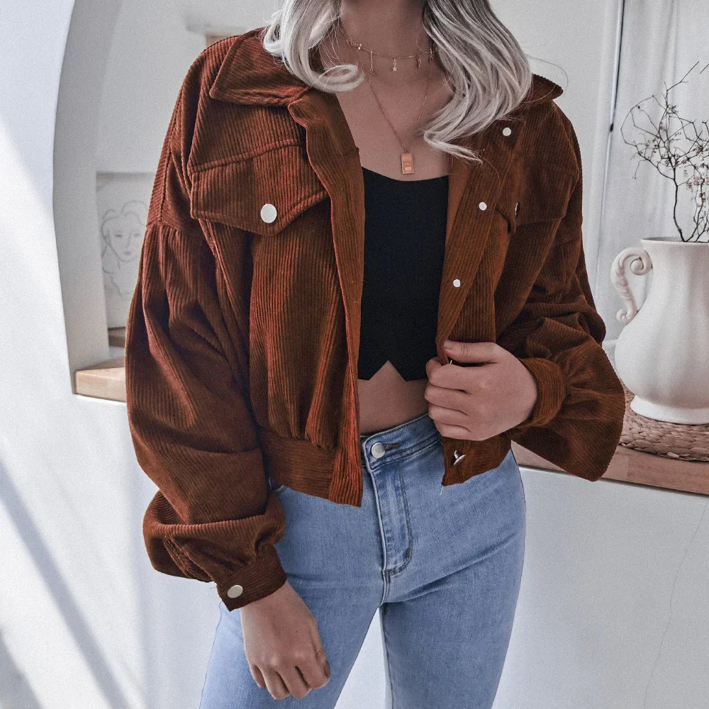 Woman wearing brown corduroy cropped jacket, black crop top, and light blue high-waisted jeans indoors