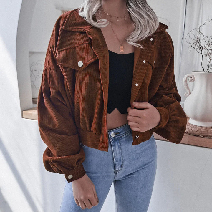 Woman wearing brown corduroy cropped jacket, black crop top, and light blue high-waisted jeans indoors