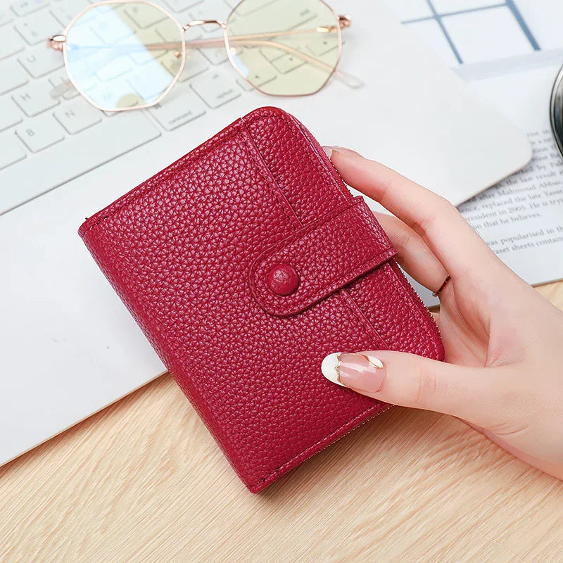 Hand holding small red textured leather wallet on wooden desk near laptop and sunglasses