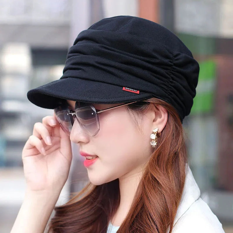 Woman wearing a black ruched cap, oversized sunglasses, and pearl drop earrings in urban setting