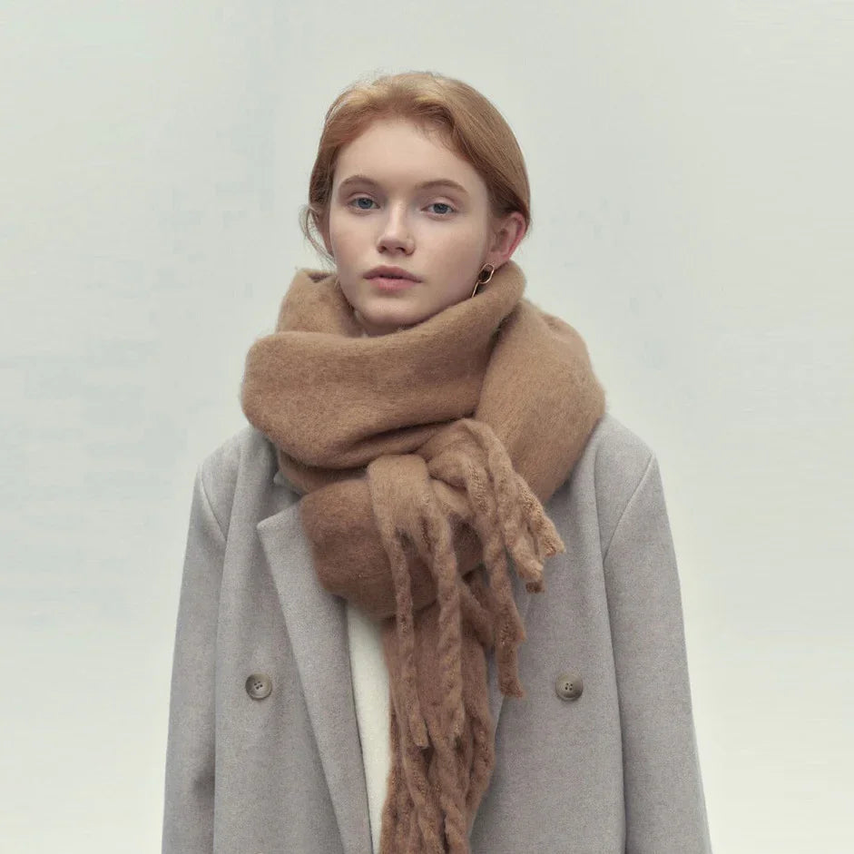 Young woman wearing oversized tan scarf and gray double-breasted coat against neutral background