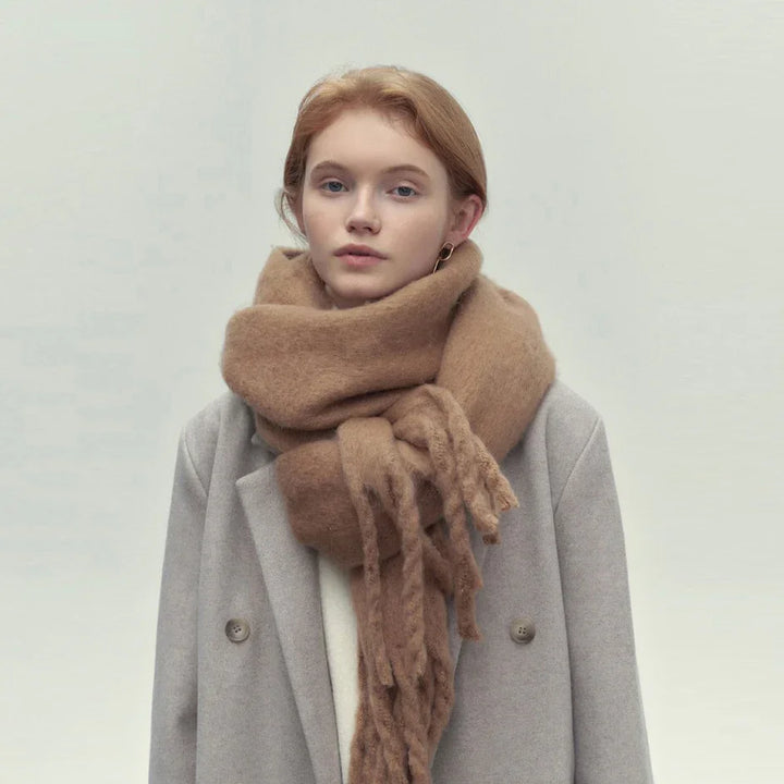 Young woman wearing oversized tan scarf and gray double-breasted coat against neutral background