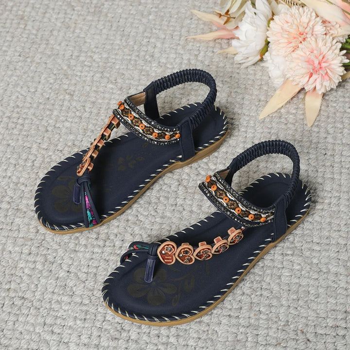 Pair of black floral embroidered women sandals with elastic back straps on textured gray surface