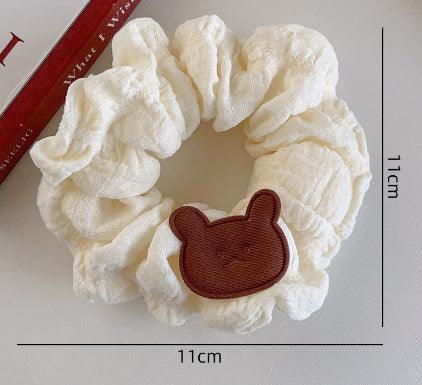 White fabric scrunchie with brown bear face patch, measuring 11cm diameter, on white surface