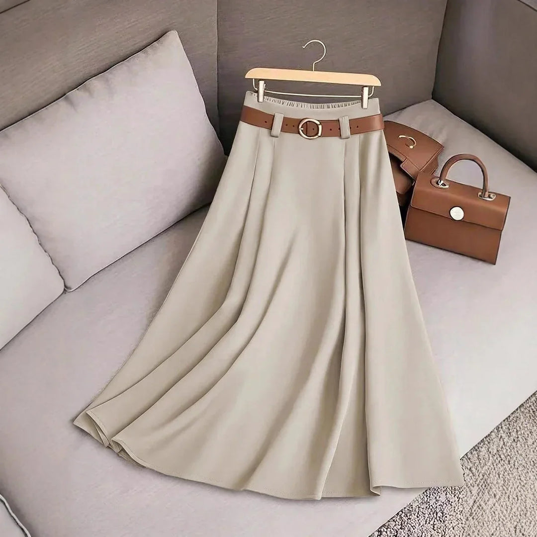 Beige pleated maxi skirt with brown belt on hanger beside brown leather handbags on couch