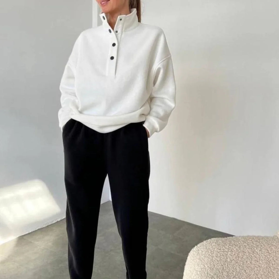 Woman wearing white buttoned pullover sweater and black pants in minimalist indoor setting