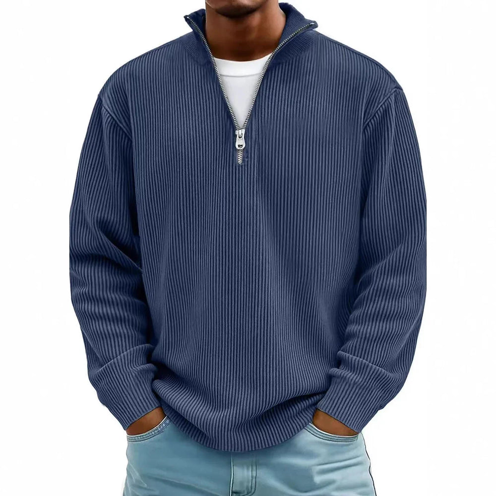 Man wearing blue ribbed quarter zip sweater with hands in light blue jeans pockets