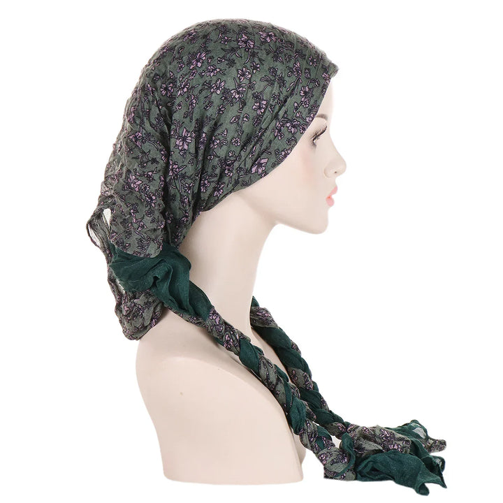Side profile of mannequin wearing green floral print headscarf with braided ends on white background