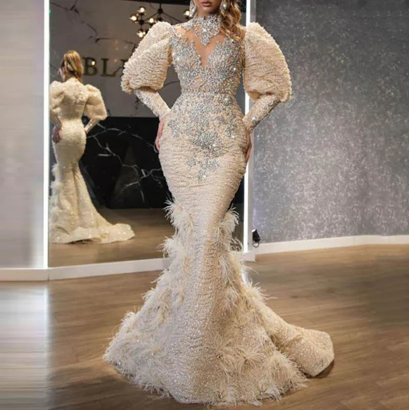Elegant beige mermaid evening gown with puffed sleeves, intricate silver embellishments, and feathered skirt detail