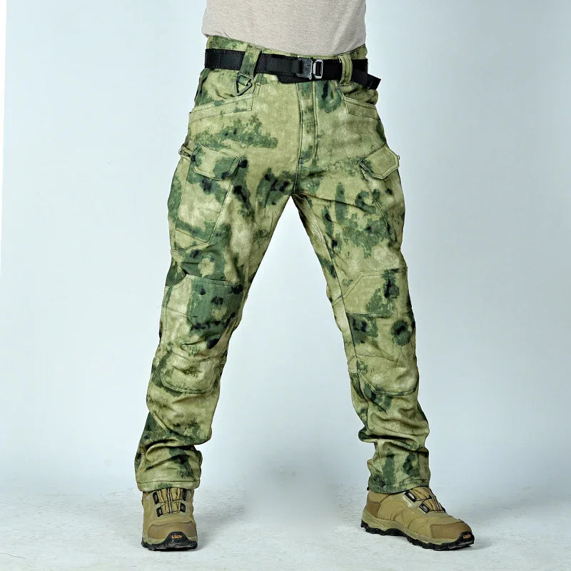Men's green camouflage tactical cargo pants with multiple pockets worn with tan hiking boots and black belt