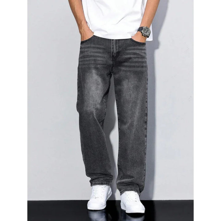 Man wearing faded black straight jeans with white sneakers and a white T-shirt against gray background