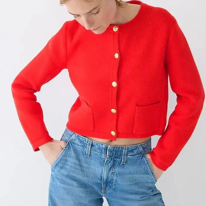 Woman wearing a bright red cropped cardigan with gold buttons and blue high-waisted jeans