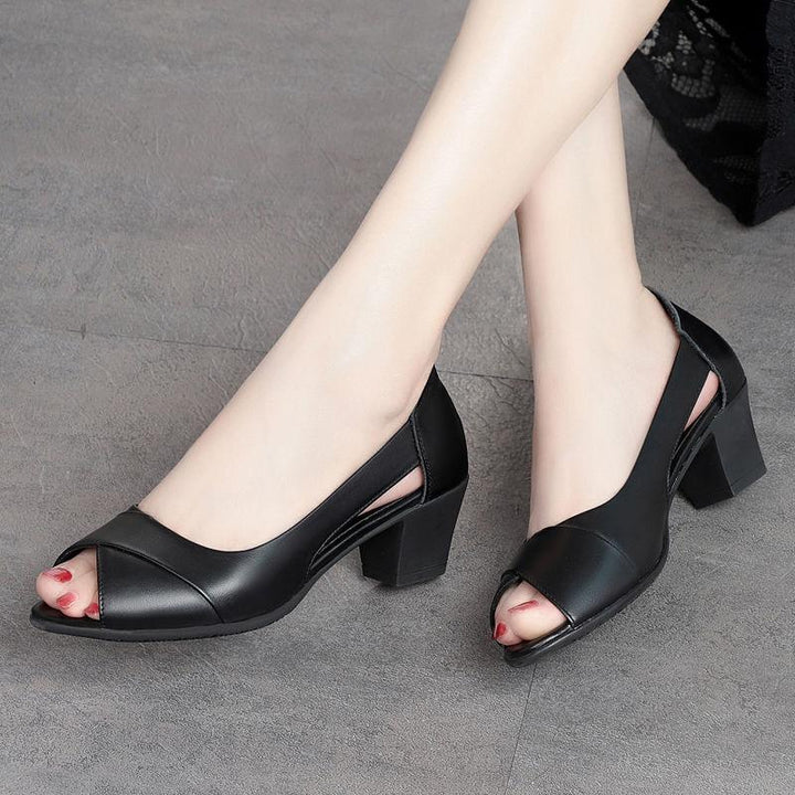 Women's black leather open-toe block heel shoes on feet against gray floor