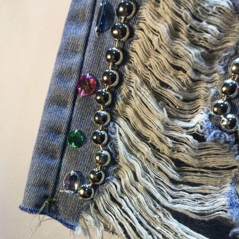 Close-up of distressed denim with silver bead chain and colorful rhinestone embellishments