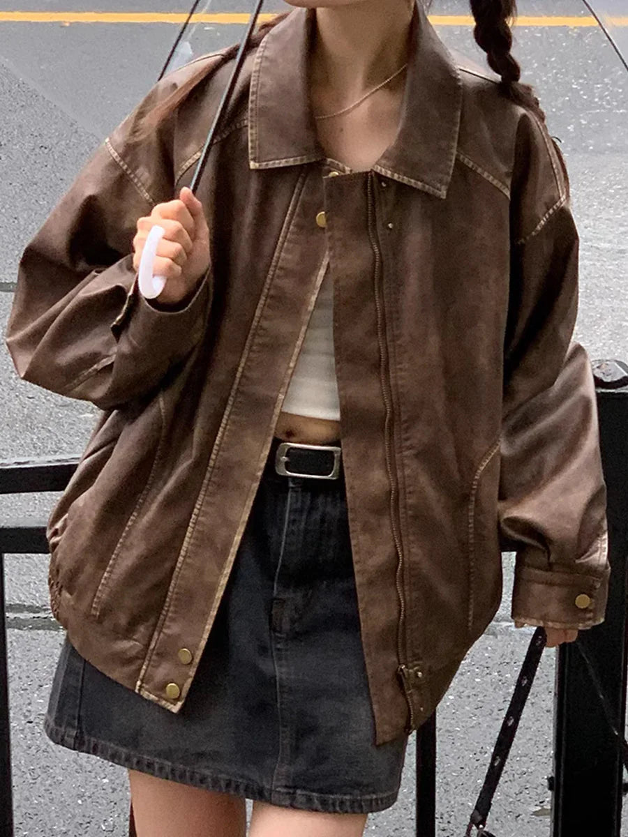 Woman wearing oversized brown leather jacket, black denim skirt, white crop top, and carrying black umbrella