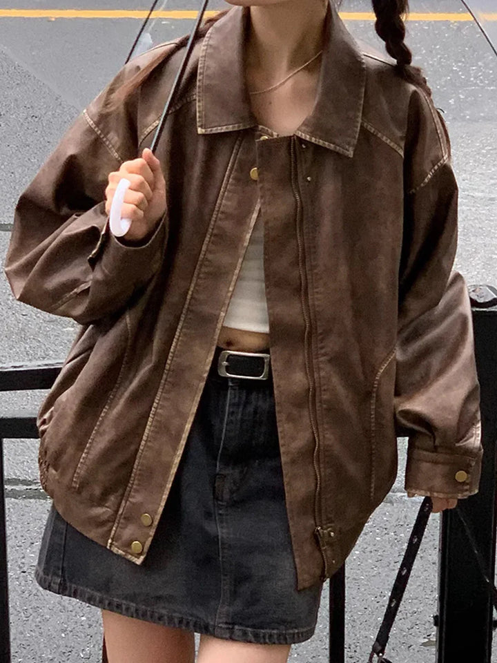Woman wearing oversized brown leather jacket, black denim skirt, white crop top, and carrying black umbrella