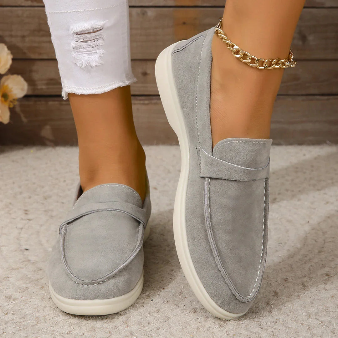 Close-up of grey suede casual loafers worn with white ripped jeans on a textured rug