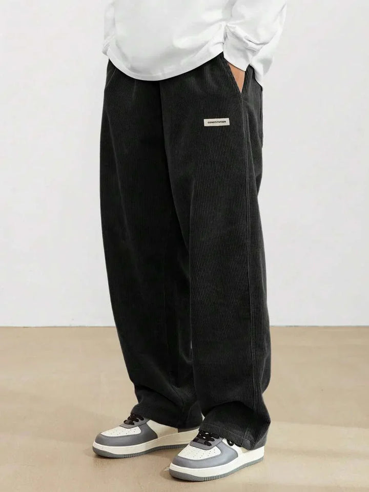 Person wearing black wide-leg corduroy pants with constitution label and gray white sneakers